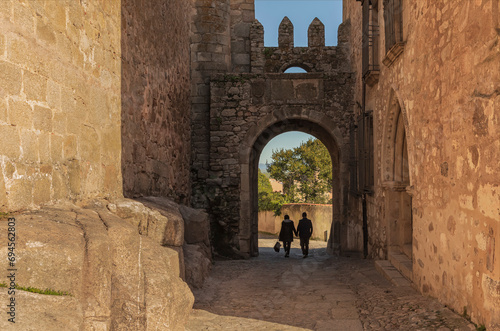 Couple holding hands walking down hill through an archway © Colleenashley