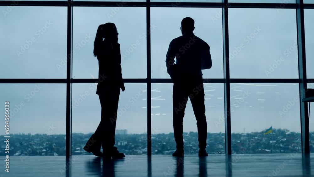 Silhouettes of business people working in the office with panoramic window. Man drinks coffee and woman has phone conversation. Silhouettes of business people working in the office with panoramic window. Man drinks coffee and woman has phone conversation.