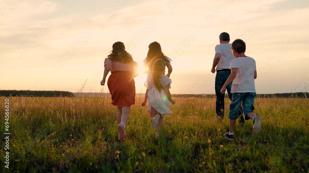Happy children with father and mother spend time on grass field at sunset. Happy family. Children with parents run across field. Children parents playfully enjoy time spent together on weekend on park