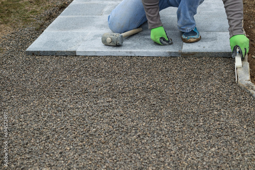 craftsman measures curbstone with folding rule while busy laying stone slabs for the walkway