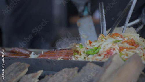 This video shows sausages and peppers being grilled on a flat top with spatulas. 