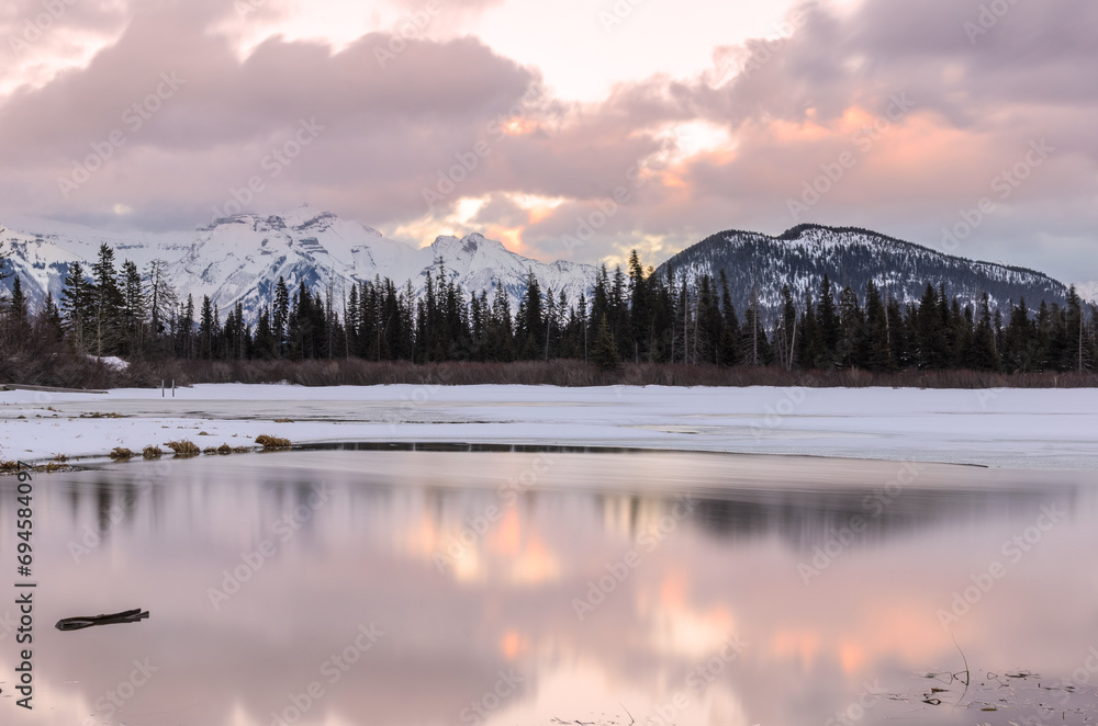 Frozen mountain lake with snow-capped mountains in background at sunset in winter Frozen mountain lake with snow-capped mountains in background at sunset in winter
