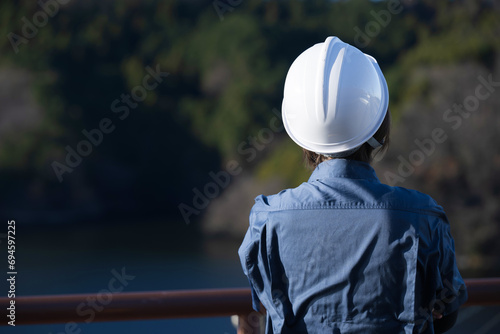 No back view of a middle-aged female site foreman staring into the future wearing a helmet, an image of career change and hiring.