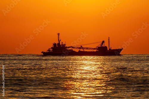夕日を浴びながらサンロードの上を進む貨物船の情景