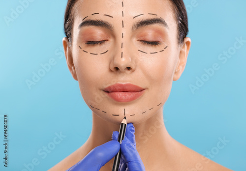 Obraz na plátně Doctor drawing marks on woman's face for cosmetic surgery operation against ligh