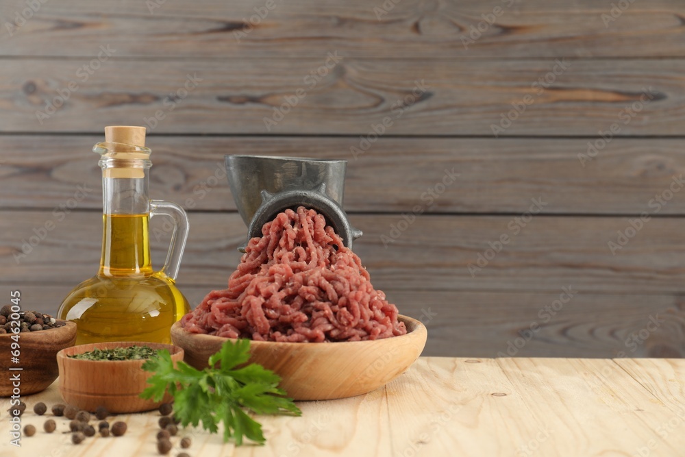 Mincing beef with manual meat grinder. Parsley, oil and spices on wooden table, space for text