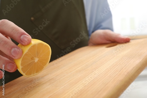 Φωτογραφία Man rubbing wooden cutting board with lemon on light background, closeup