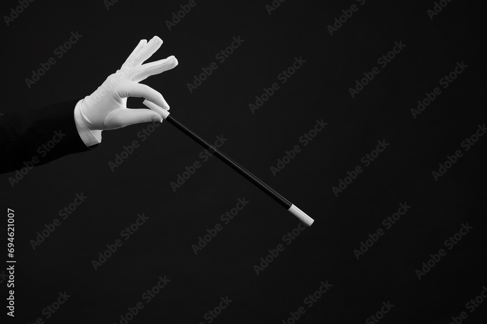 Fototapeta premium Magician holding wand on black background, closeup. space for text