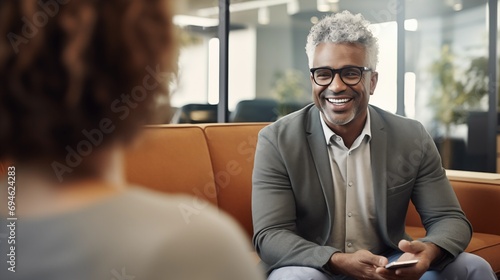 A 40s year old Afro male financial advisor in short grey hair with glasses counseling a woman in modern office.