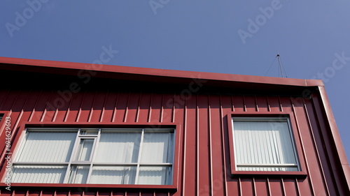 Rectangular windows on red corrugated facade against blue sky, facade corner