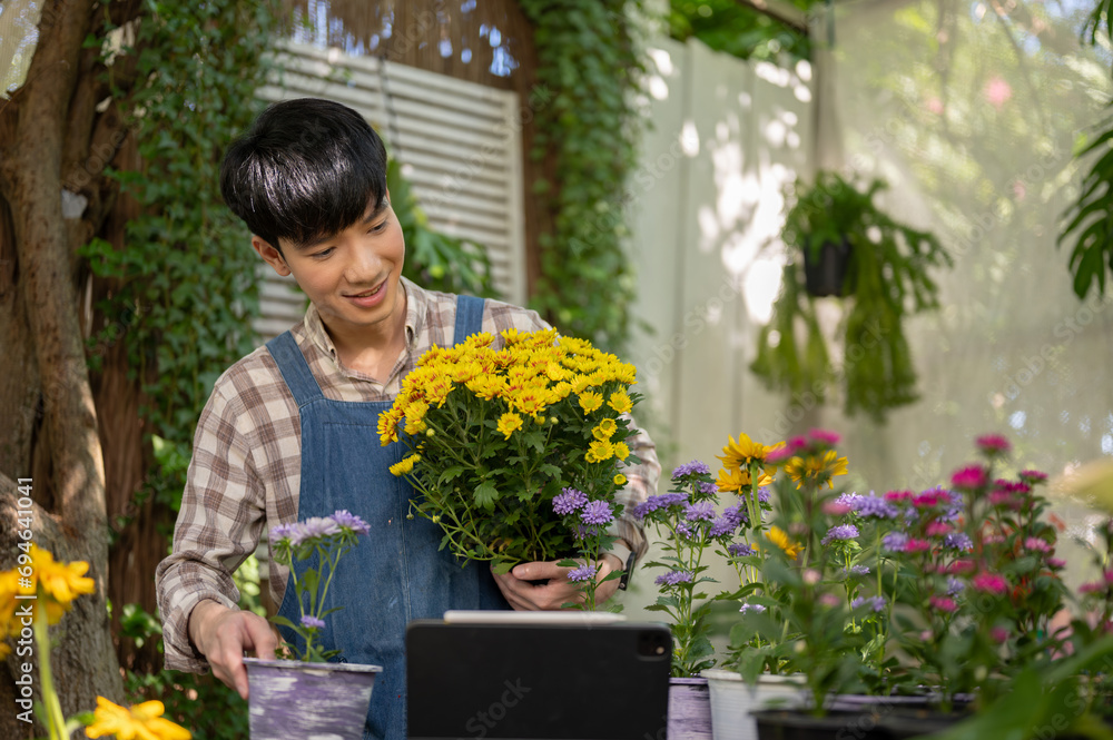 A happy and handsome young Asian male florist or gardener is working in a plant nursery in a garden.