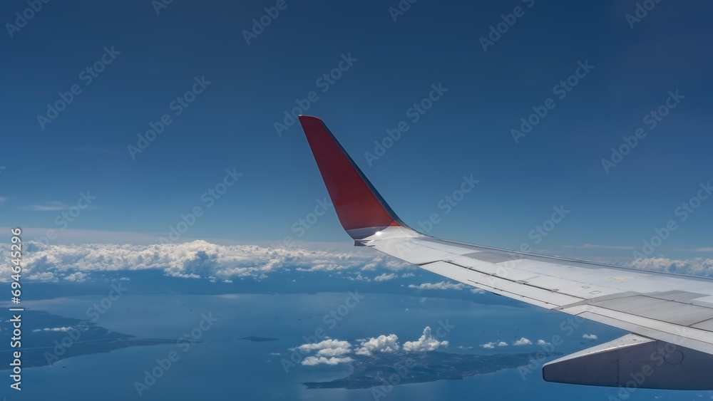 Fototapeta premium The aerial view from the plane to Malaysia. Tropical islands in the blue ocean. Clouds in the azure sky. The wing of the aircraft is in the foreground. Copy space. 