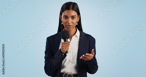 Woman, portrait or presenter in studio talking, speaking on talk show or media on blue background. Breaking news, tv press or Indian reporter presenting live global political events with microphone photo