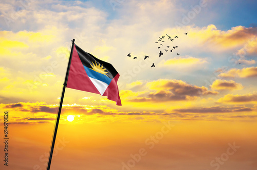 Waving flag of Antigua and Barbuda against the background of a sunset or sunrise. Antigua and Barbuda flag for Independence Day. The symbol of the state on wavy fabric.