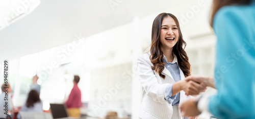 Shot of two businesswomen shaking hands in an office. Two smiling businesswomen shaking hands while standing in an office. Business people shaking hands, finishing up a meeting photo