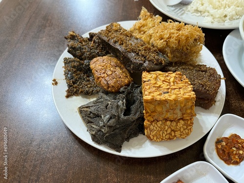 A plate of side dish consists of fried tempeh, cow beef, Potato Perkedel, and Empal in a restaurant photo