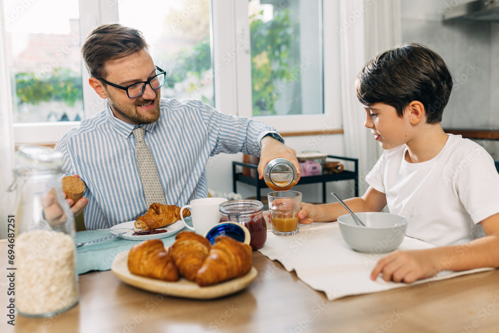 Man is pouring juice for his son. They eat breakfast together. Man is pouring juice for his son. They eat breakfast together.