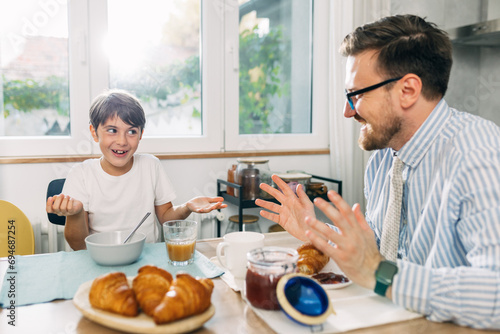 Cheerful boy and his father have fun talking during breakfast at home.