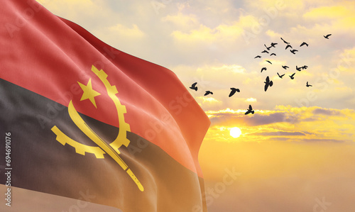 Waving flag of Angola against the background of a sunset or sunrise. Angola flag for Independence Day. The symbol of the state on wavy fabric. photo