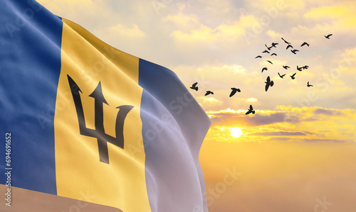 Waving flag of Barbados against the background of a sunset or sunrise. Barbados flag for Independence Day. The symbol of the state on wavy fabric.