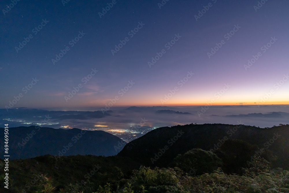 Early morning night sky from the top of Doi Luang Chiang Dao in Chiang Mai, Thailand overlooking a glowing town lights and beautiful dark blue sky