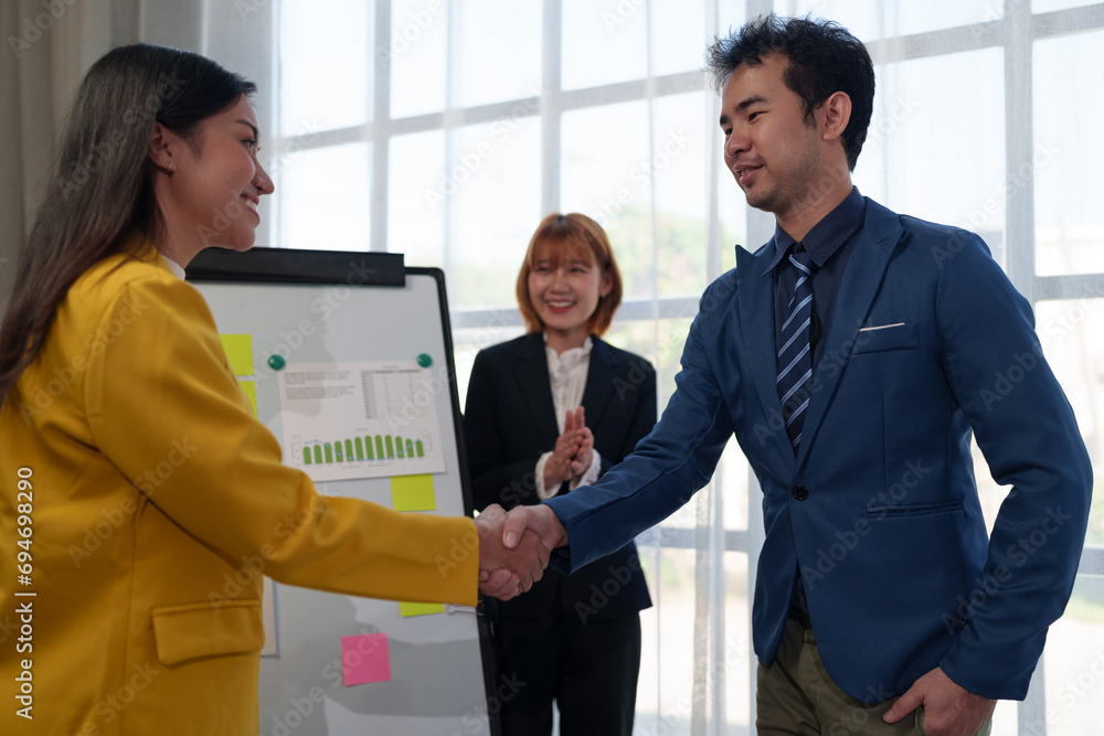 Two Asian business partners holding hands succeeding together in front of applauding colleagues in modern office Partner approval and appreciation of successful business goal idea. Two Asian business partners holding hands succeeding together in front of applauding colleagues in modern office Partner approval and appreciation of successful business goal idea.