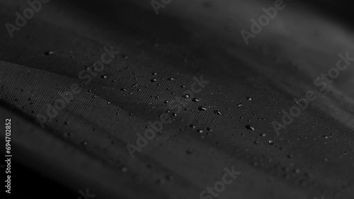 Raindrops on the black material of a closed umbrella. Wet dark textile with water drops. Rainy season concept. Rotation photo