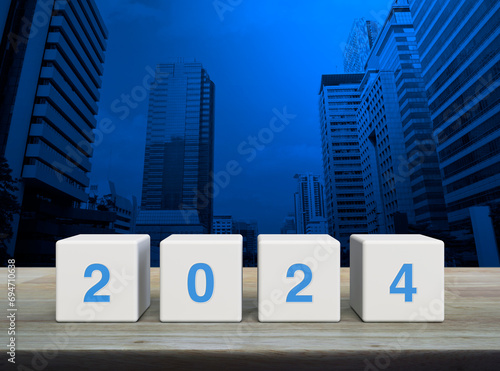 2024 letter on white block cubes on wooden table over modern office city tower and skyscraper, Happy new year 2024 cover concept