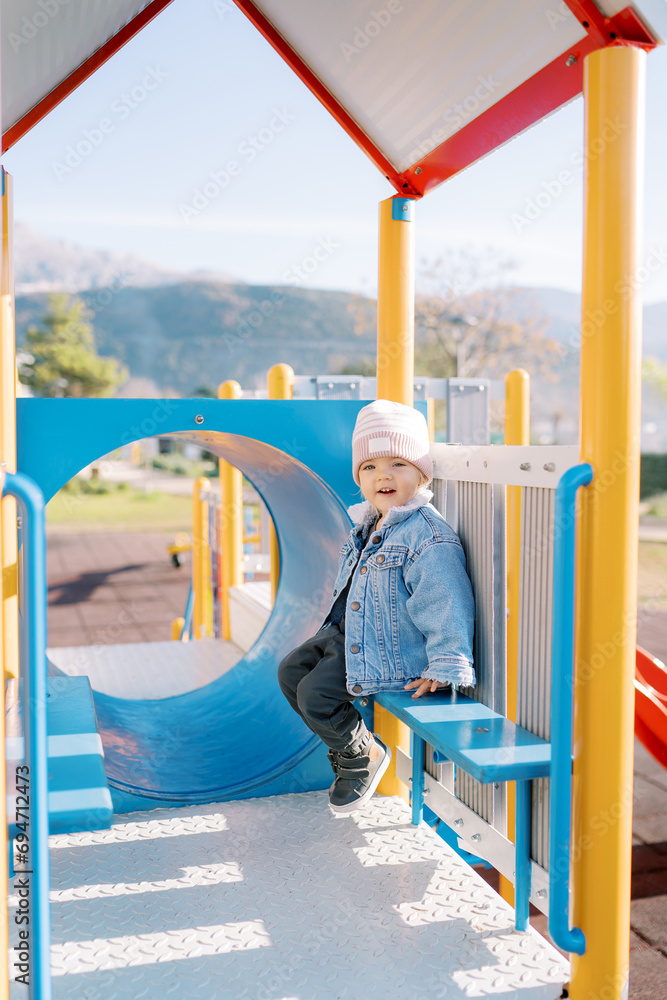 Little smiling girl sitting on a bench on a slide