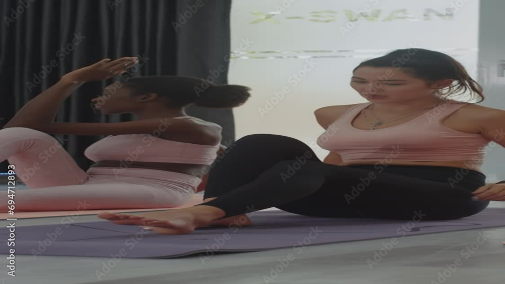 Vertical shot of African American and Caucasian women practicing half spinal twist stretching at fitness studio Vertical shot of African American and Caucasian women practicing half spinal twist stretching at fitness studio