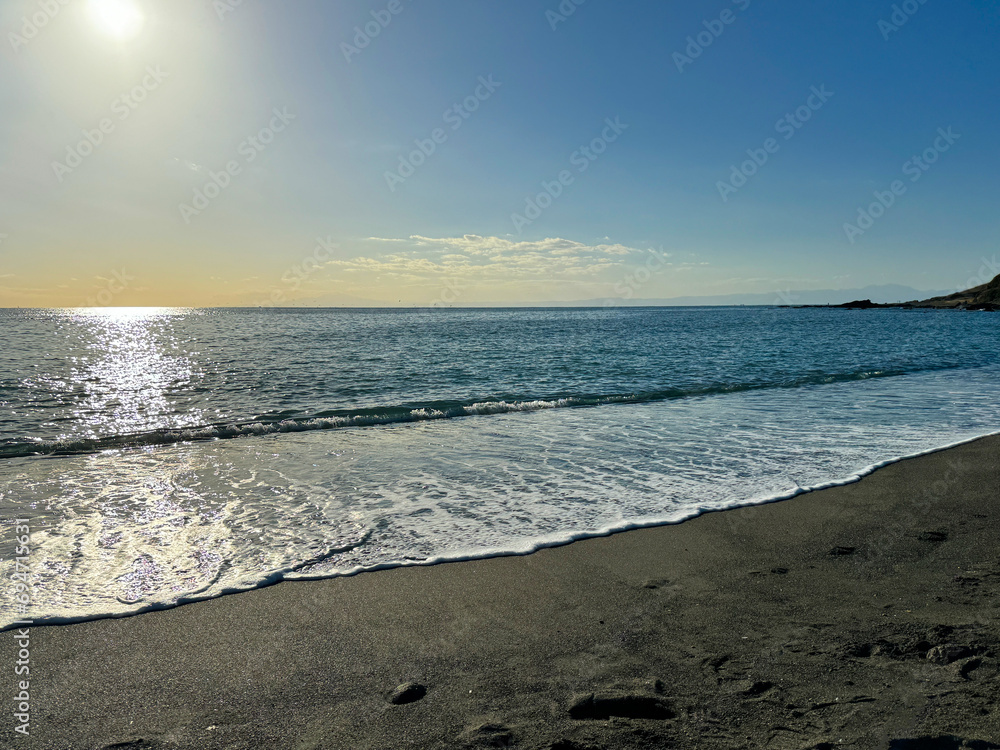 Obraz premium 大きな海に波が打ち寄せ、青い大空と太陽と夕日が混ざり合い、高台から見下ろす実写写真