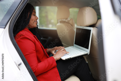 beautiful african passenger in the back seat of a car with a laptop