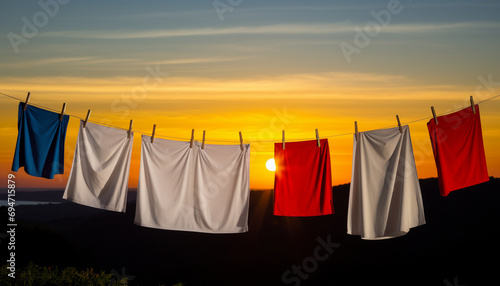 Clothes on a line against a sunset, with blue, white, and red items silhouetted