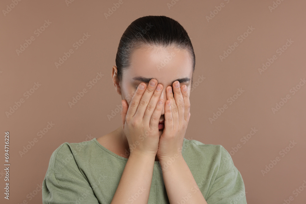 Resentful woman covering face with hands on brown background Resentful woman covering face with hands on brown background