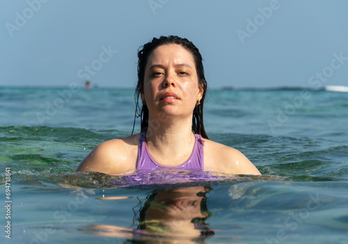 Portrait of pretty young woman swimming in the ocean, looking at camera. Bali.