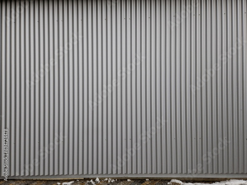building is lined with square panels. metal sheet wall cladding with scalloped design. corrugated sheet, dark gray, riveted. horizontal stripes, shadows, corner, fence, aluminium, sheet photo
