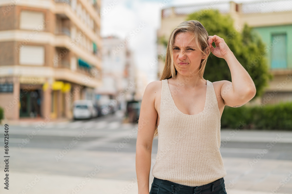 Young blonde woman at outdoors having doubts
