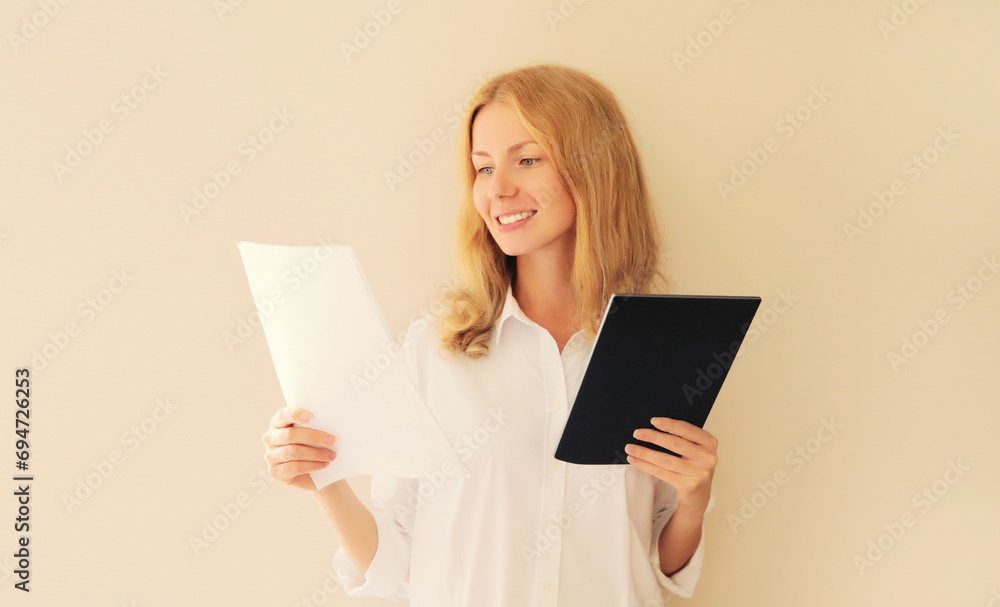 Professional caucasian young woman employee while working with digital tablet computer looking at paper document at home or office Professional caucasian young woman employee while working with digital tablet computer looking at paper document at home or office