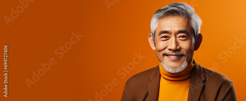Elegant smiling elderly Asian man with gray hair, on an orange background, banner, copy space, portrait.