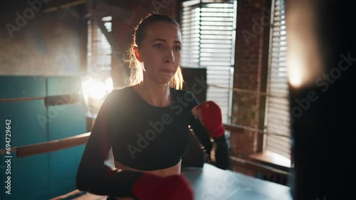 Young strong woman boxer in sportswear gives punches by hans on boxing ring. Training, workout and professional sport concept. Self-defence, girls power, womans power and prepares to fight, feminism. photo