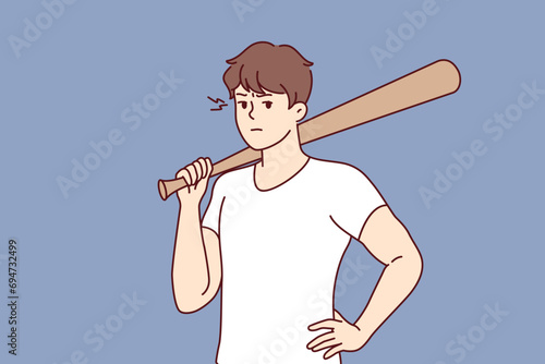 Hooligan guy with baseball bat in hand stands with hand on belt and threatens to beat up passerby. Male hooligan or gangster uses stick to intimidate people and extort or rob store