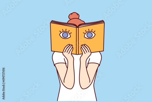 Woman covers face with book from bookstore, reading interesting textbook with giant eyes on cover. Teenage bookworm girl enjoys studying library book with shocking facts and mesmerizing stories