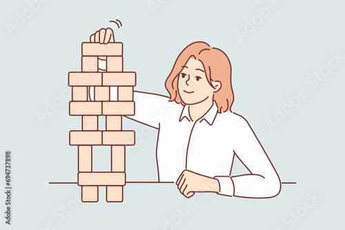 Business woman builds tower of wooden cubes, symbolizing sustainable business strategy and working on development of company. Girl in business clothes plays board game developing concentration.