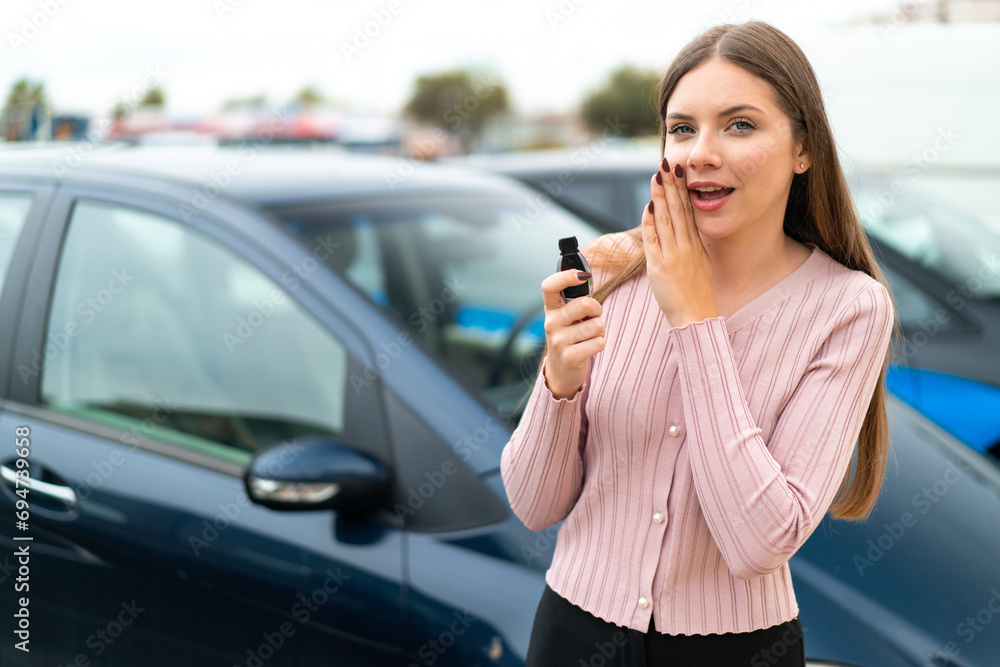 Young pretty blonde woman holding car keys at outdoors whispering something Young pretty blonde woman holding car keys at outdoors whispering something