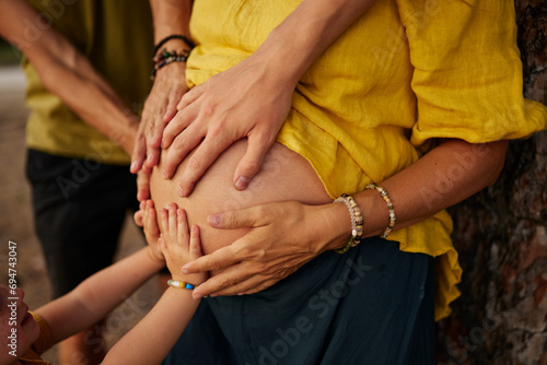 Family touching pregnant woman's stomach in park photo