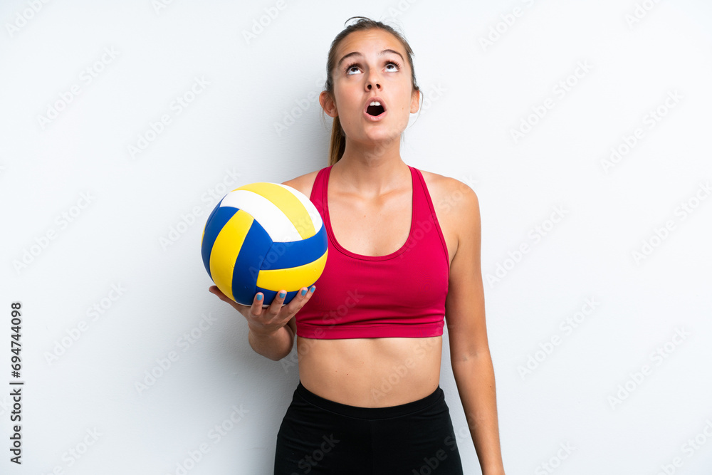 Young caucasian woman playing volleyball isolated on white background looking up and with surprised expression Young caucasian woman playing volleyball isolated on white background looking up and with surprised expression