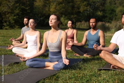 Group of people practicing yoga on mats outdoors. Lotus pose