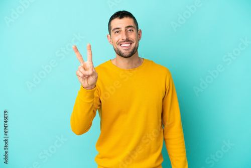 Young handsome caucasian man isolated on blue background smiling and showing victory sign