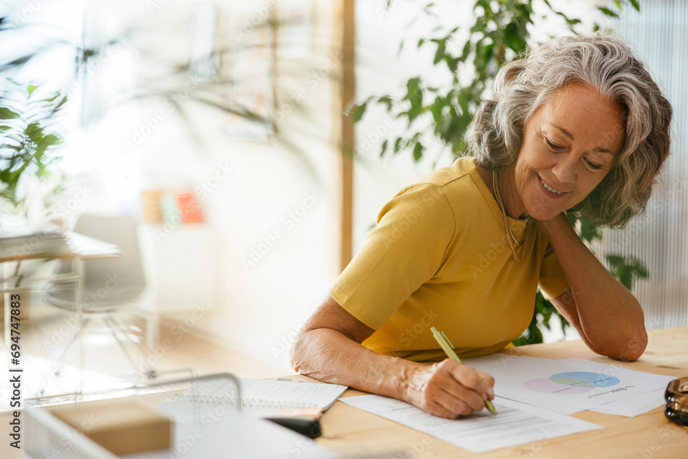 Smiling businesswoman writing on document at desk in office Smiling businesswoman writing on document at desk in office