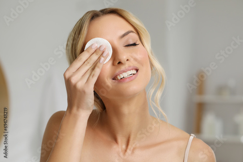 Smiling woman removing makeup with cotton pad indoors photo